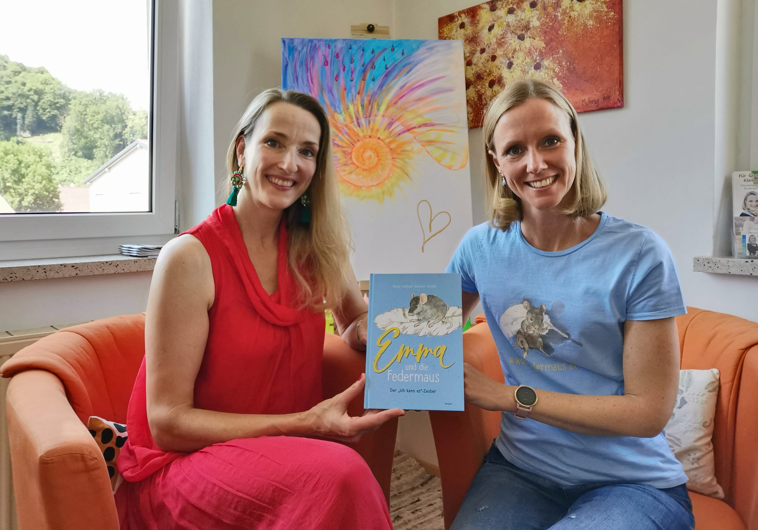 Margit & Annette sitzen am Sofa und zeigen das Federmaus-Buch her